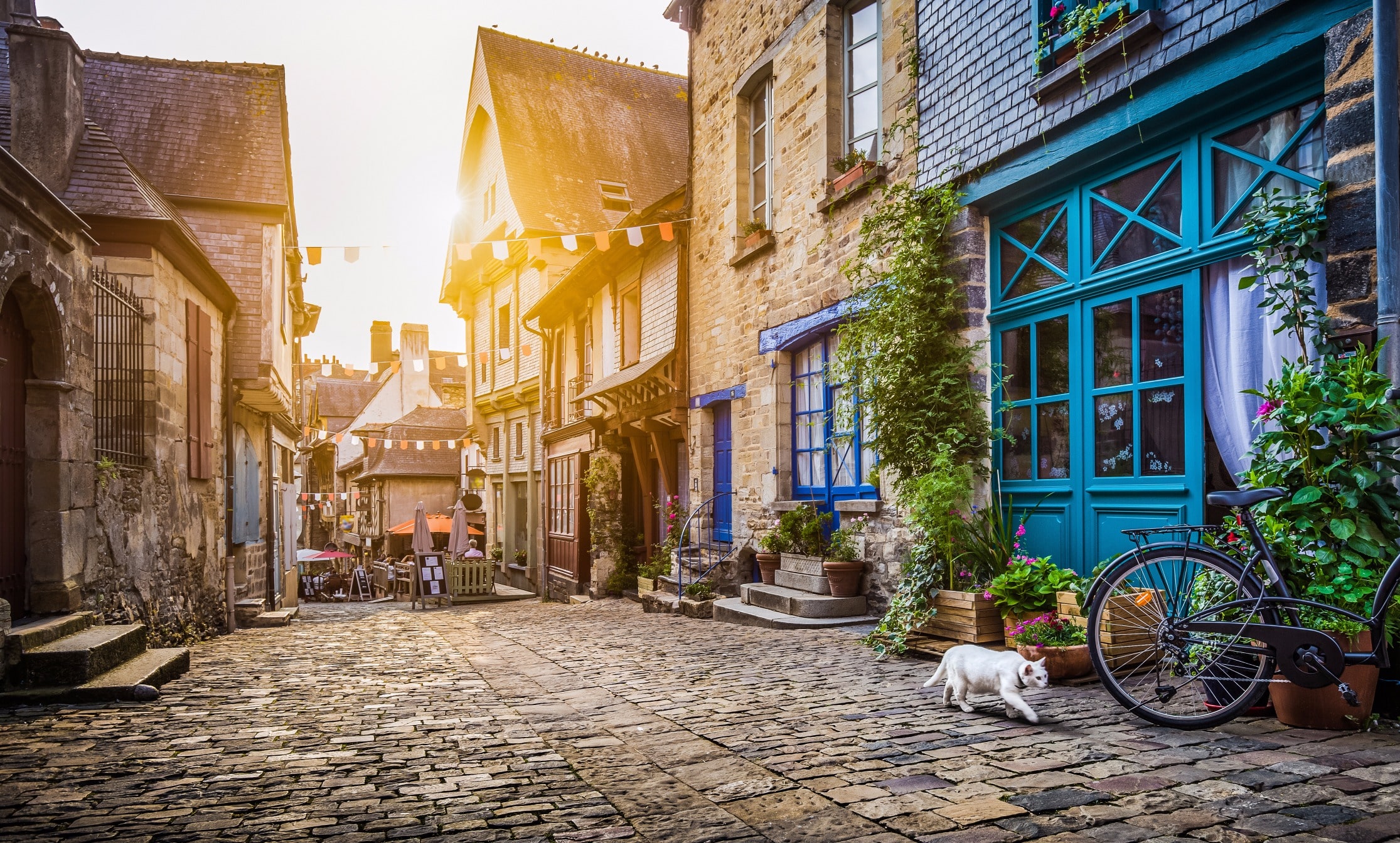 A sunny European city street with historic townhouses and café terraces